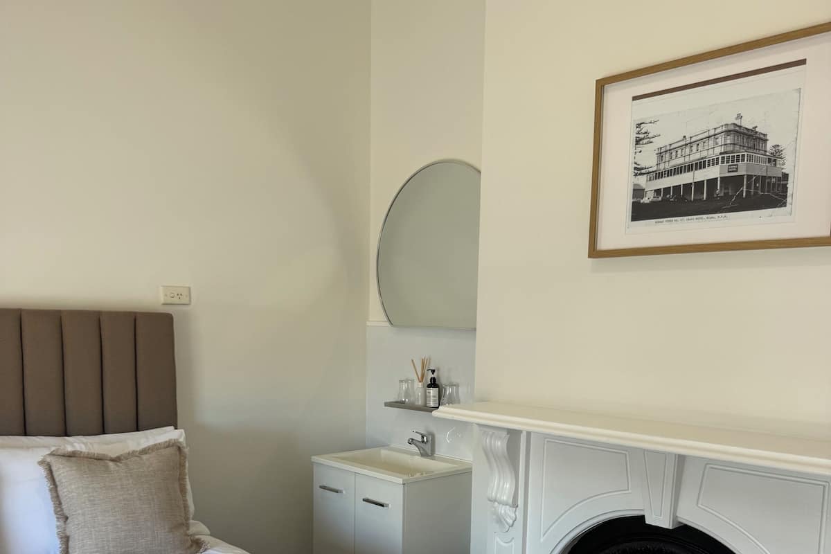 Une chambre d’hôtel avec un lit, une petite table de chevet, un miroir, un tableau encadré au mur et une cheminée.