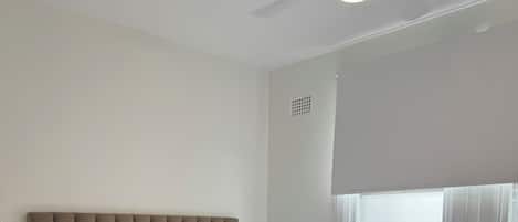 Un lit bien fait, avec une tête de lit grise, du linge de lit blanc et un plaid marron.