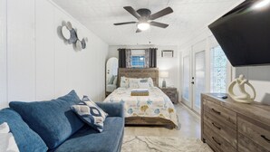 A bedroom with a bed, a blue sofa, a wooden dresser, and a ceiling fan. - Guesthouse by the Beach (Fort Pierce)