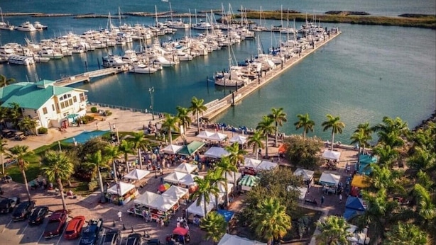 A marina with numerous boats docked, a parking area with cars, and a small building with a green roof. - Guesthouse by the Beach (Fort Pierce)