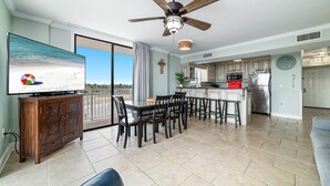 A spacious living room with a large flat-screen TV, a ceiling fan, and a dining area with a table and chairs. - Seaside Beach & Racquet Club 3301 – Beachfront w Pool! 🌊☀️ (Orange Beach)