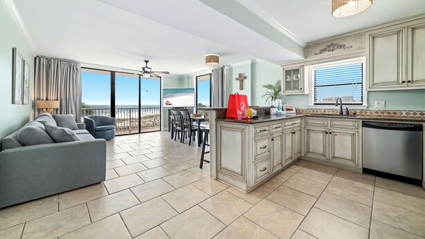 A spacious living area with a gray sofa, a dining table with chairs, a kitchen with light-colored cabinets, and a view of the ocean through large windows. - Seaside Beach & Racquet Club 3301 – Beachfront w Pool! 🌊☀️ (Orange Beach)