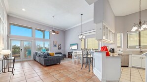 En rummelig opholdsstue med en grå sofa, et spisebord og et køkkenområde med hvide skabe og en bardisk.