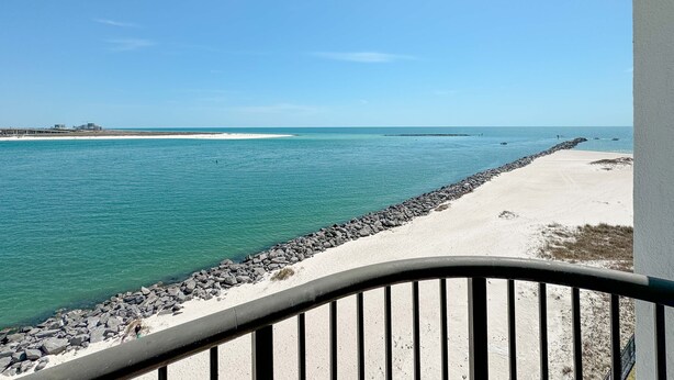 Vista costera con playa arenosa, mar tranquilo y un rompeolas rocoso.