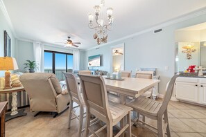 A dining area with a light wooden table, beige chairs, a chandelier, and a ceiling fan. - BEACHFRONT, FAMILY FRIENDLY, LOW FLOOR, INDOOR/OUTDOOR POOL | BEACHBALL PROPERTIES (Orange Beach)