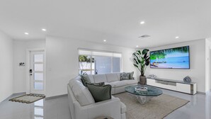 Una sala de estar moderna con un sofá blanco, una mesa de centro de vidrio y un televisor grande en la pared.