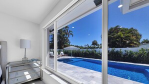 Una habitación moderna con un amplio ventanal con vistas a una piscina, un aparador de vidrio y una lámpara.
