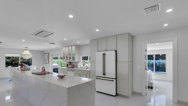 Una cocina moderna con una isla de mármol, armarios blancos y un refrigerador grande.