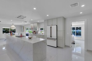 Una cocina moderna con una isla de mármol, armarios blancos y un refrigerador grande.
