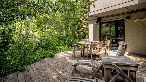 A wooden deck with outdoor furniture, surrounded by dense greenery. - Andora Alpine Retreat - 2BD in downtown Ketchum (Ketchum)
