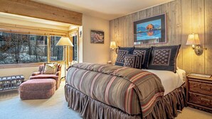 A bedroom with a large bed, a view of trees through a window, and a painting on the wall. - Andora Alpine Retreat - 2BD in downtown Ketchum (Ketchum)