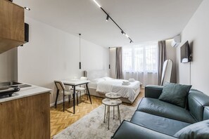 A modern, well-lit room with a kitchenette, a bed, a sofa, and a dining area. - Cozy Studio - Serenitas 2 City Center (Tirana)