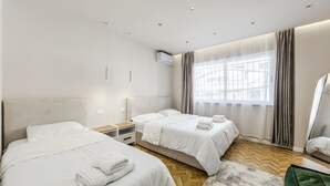 A hotel room with two beds, a wooden floor, a large window with curtains, and an air conditioning unit. - 1 Bedroom Loft - Serenitas 1 (Tirana)