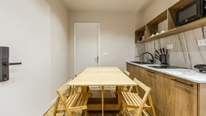 A compact kitchen with a wooden table and chairs, a microwave, and a marble backsplash. - 1 Bedroom Loft - Serenitas 1 (Tirana)