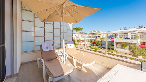 Un balcon avec une table et des chaises, un grand parasol et une vue sur d’autres immeubles.
