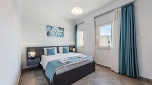Une chambre moderne avec un grand lit, des tables de chevet avec des lampes, une fenêtre avec des rideaux et un luminaire au plafond.