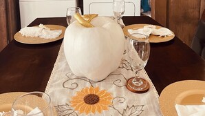 A dining table with a white pumpkin centerpiece, surrounded by plates and glasses, set against a wooden wall with laundry-themed decorations.