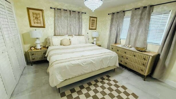 A bedroom with a large bed, two bedside tables, a dresser, and a chandelier.