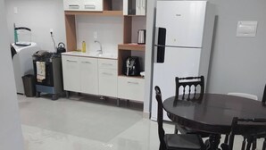 A modern kitchen with white cabinets, a built-in oven, and a coffee maker. There is a dining area with a round table and chairs.