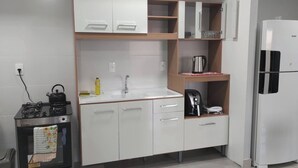 A modern kitchen with white cabinets, a stainless steel kettle, a coffee maker, and a refrigerator.