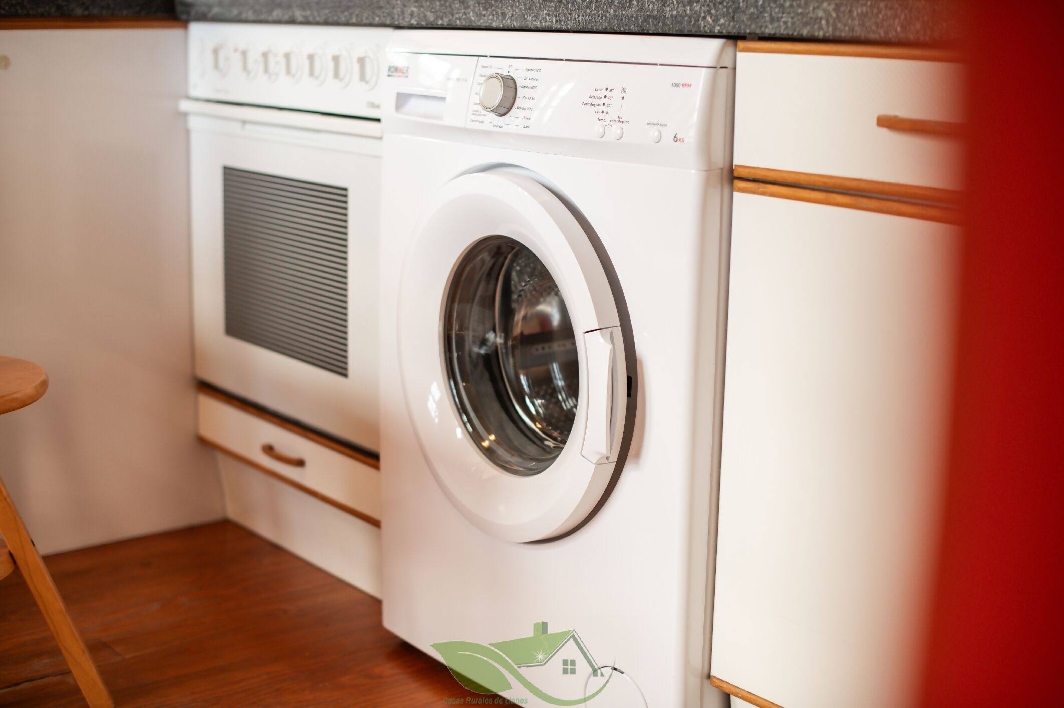 A front-loading washing machine in a kitchen with wooden cabinets and a countertop.