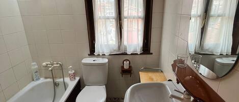 A bathroom with a bathtub, toilet, and sink, featuring a window with curtains, a towel rack, and a mirror.
