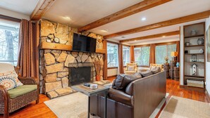 A cozy living room with a stone fireplace, wooden beams, a comfortable sofa, and a bookshelf. - Portage Lakes, Lakefront, Private Dock & Deck (Akron)