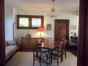Uma sala de jantar com mesa e cadeiras de madeira, um candelabro, uma janela com vista e uma porta.