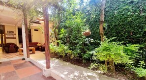 Un patio con piso a cuadros, mobiliario de madera y abundante vegetación.