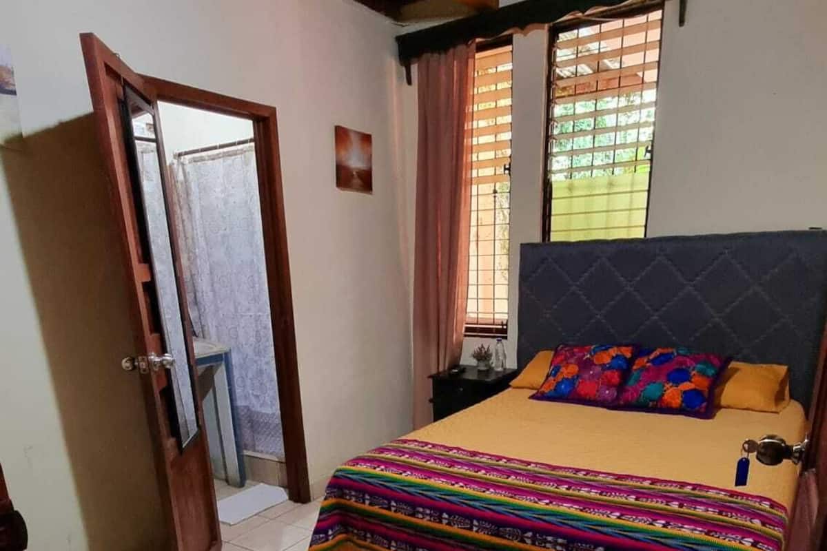 Une chambre à coucher avec un lit, une fenêtre avec des rideaux, une porte et un sol carrelé.