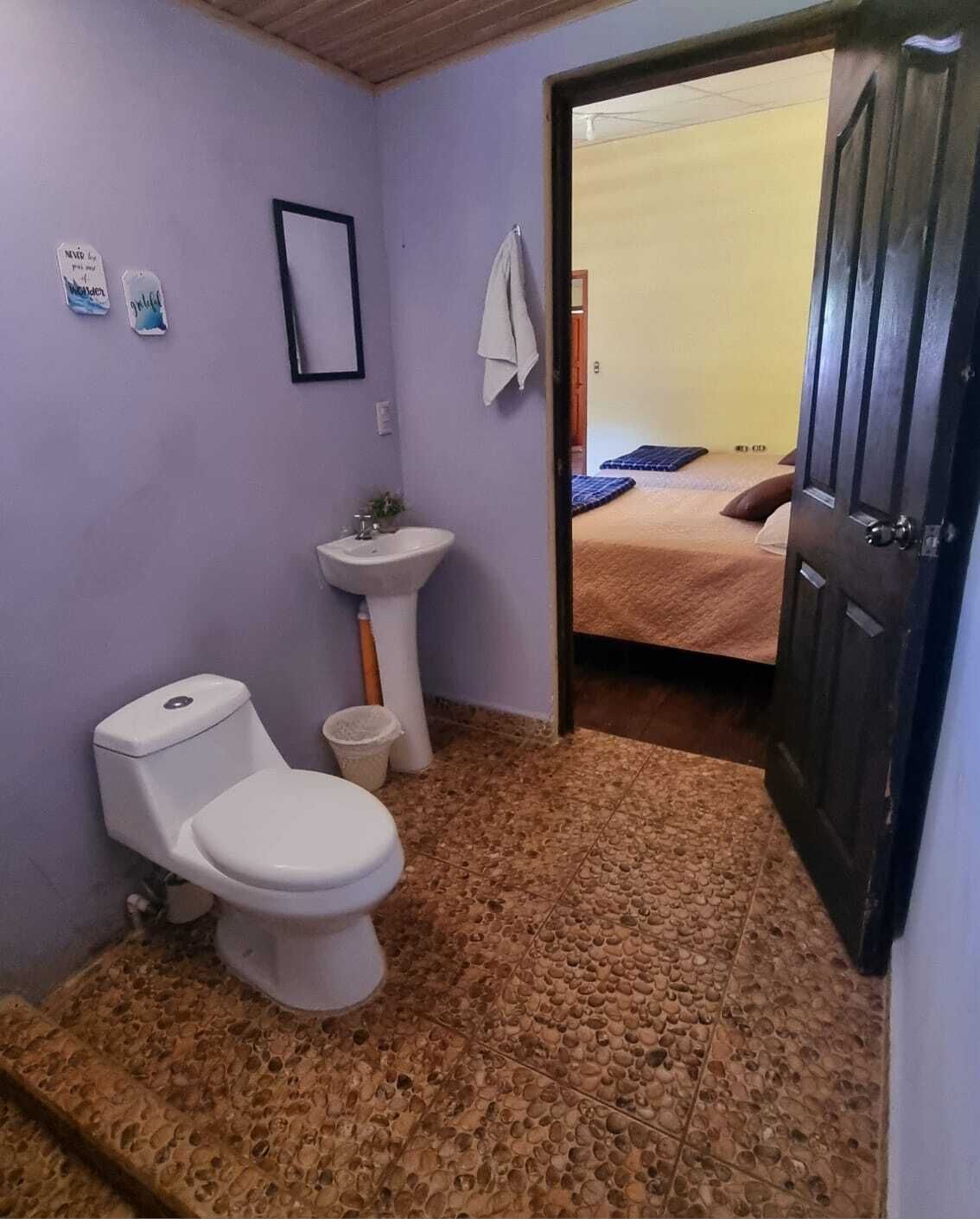 Un baño pequeño con inodoro, lavamanos y una puerta que da a un dormitorio.