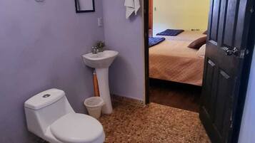 Un baño pequeño con inodoro, lavamanos y una puerta que da a un dormitorio.