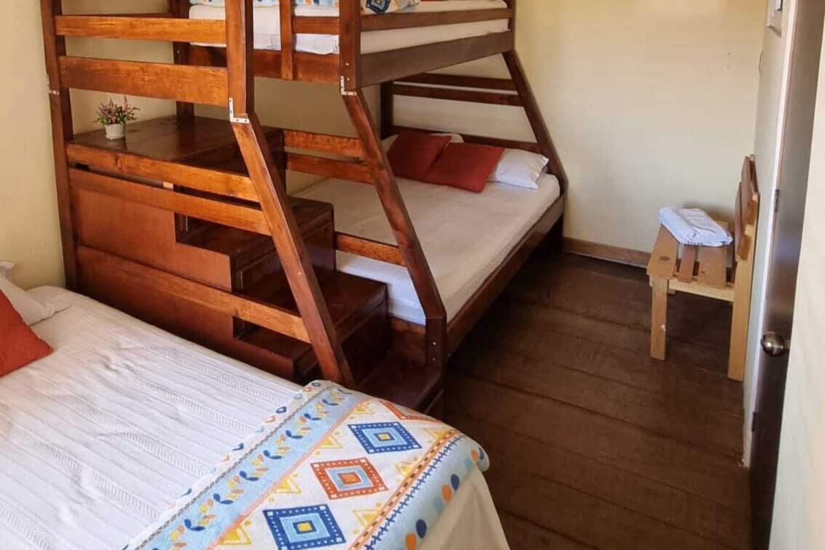 Une chambre avec des lits superposés, un petit tabouret et un lit recouvert d’une courtepointe à motifs.