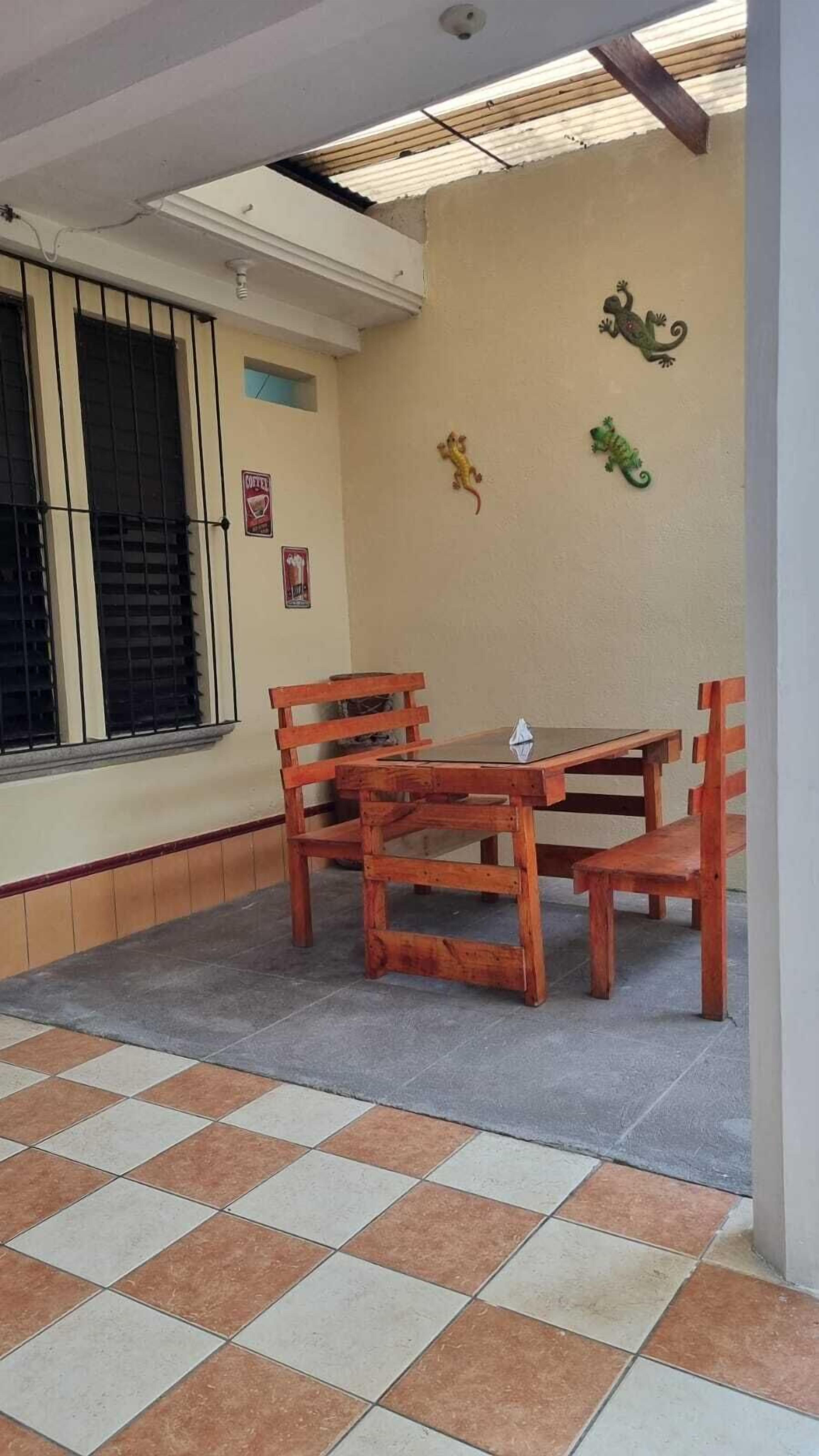 Una habitación con piso de baldosas, una mesa y sillas de madera, una ventana con rejas y decoración en la pared.