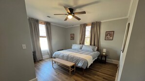 A bedroom with a bed, a bench, a ceiling fan, and two windows with curtains. - Historic Downtown Somerset. Newly Renovated. 3 Kings. Two blocks to fountain. (Somerset)