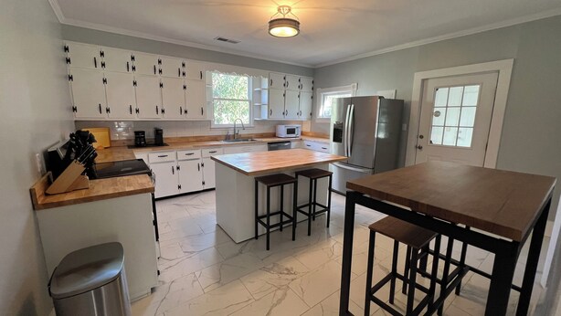 A modern kitchen with white cabinets, a stainless steel refrigerator, a wooden island, and a bar stool seating area. - Historic Downtown Somerset. Newly Renovated. 3 Kings. Two blocks to fountain. (Somerset)