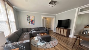 A modern living room with a sectional sofa, a round coffee table, a flat-screen TV, and a dining area with a wooden table and chairs. - Historic Downtown Somerset. Newly Renovated. 3 Kings. Two blocks to fountain. (Somerset)