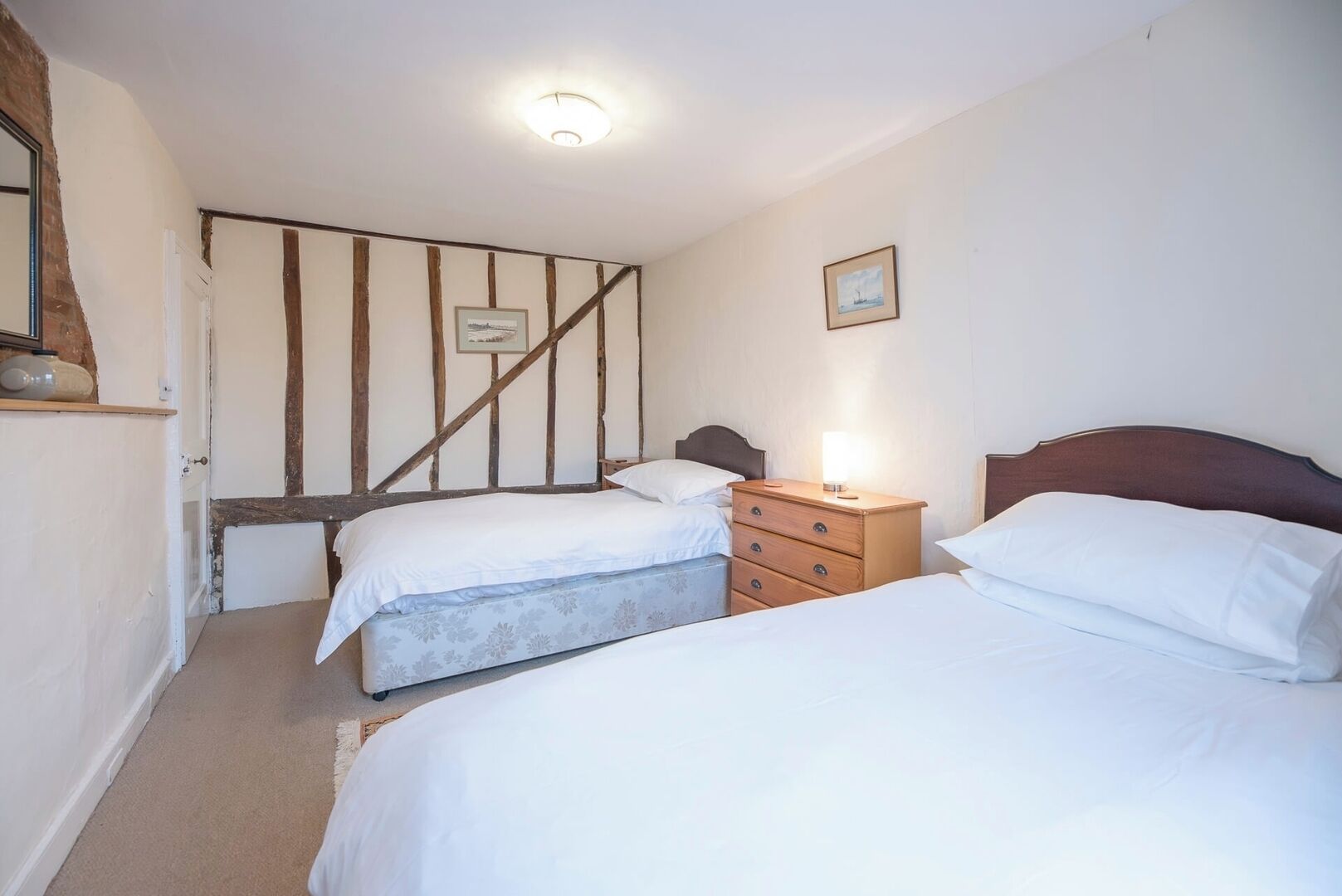 Een slaapkamer met twee bedden, een houten dressoir en een ingelijst schilderij aan de muur.