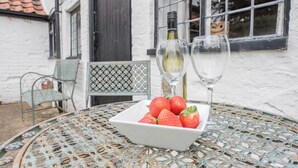 A table with a bowl of strawberries and two wine glasses, set outdoors in front of a white building with a window and a door. - Varley House, Saxmundham (Saxmundham)