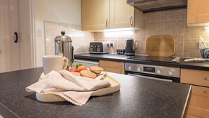 A modern kitchen with wooden cabinets, a black countertop, a coffee maker, a toaster, and a plate with cookies and strawberries. - Varley House, Saxmundham (Saxmundham)