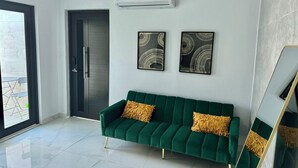 Ein modernes Wohnzimmer mit einem smaragdgrünen Samtsofa, zwei golden verzierten Kissen und zwei abstrakten Wandbildern.