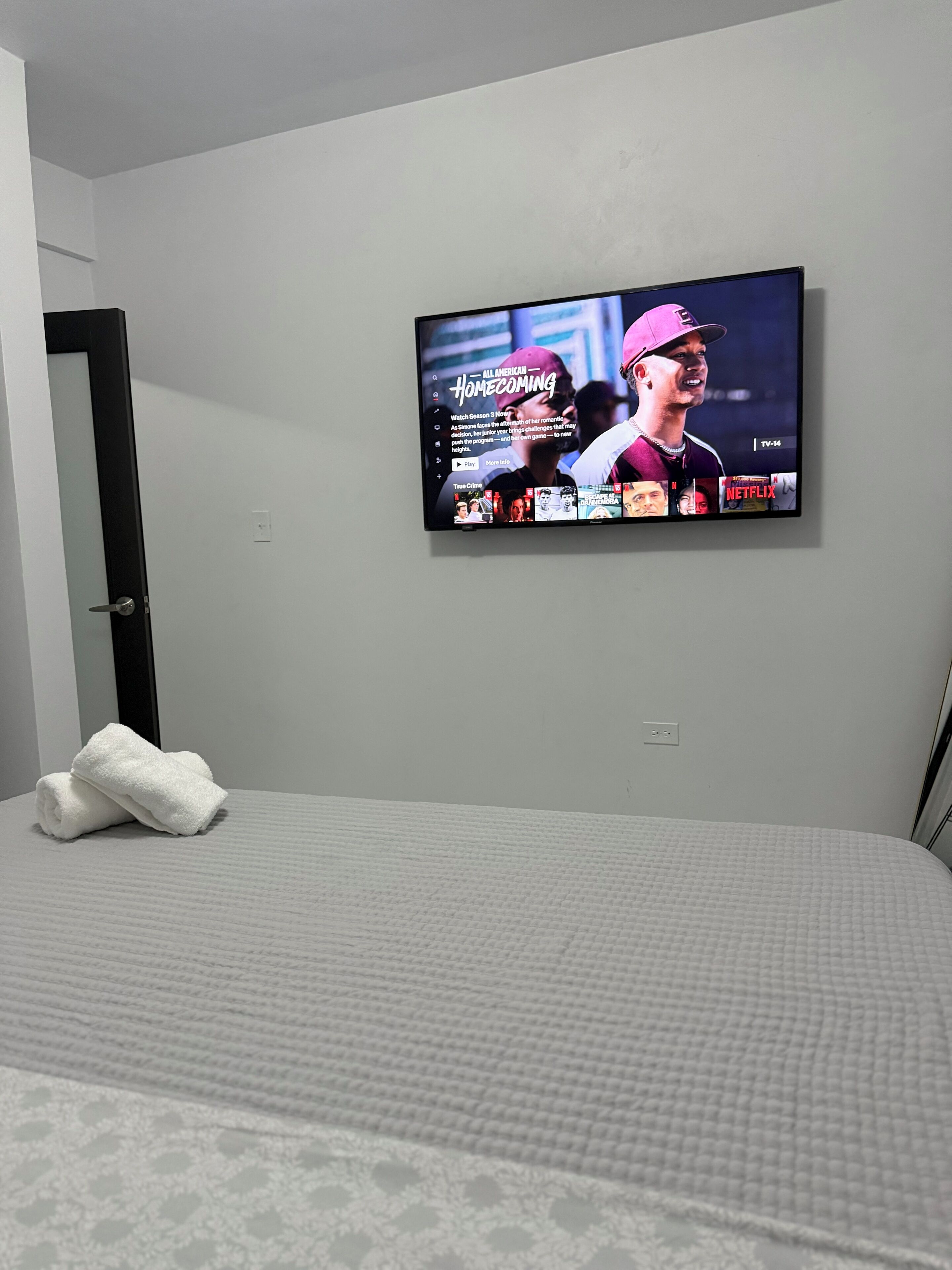 A bedroom with a bed, a TV mounted on the wall, and a white towel on the bed.