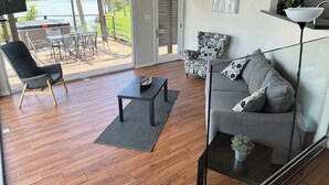 A modern living room with a grey sofa, a black coffee table, and a wooden floor. There is a glass door leading to an outdoor patio with a table and chairs. - Riverfront Home in Houston with private pool and hot tub (Houston)