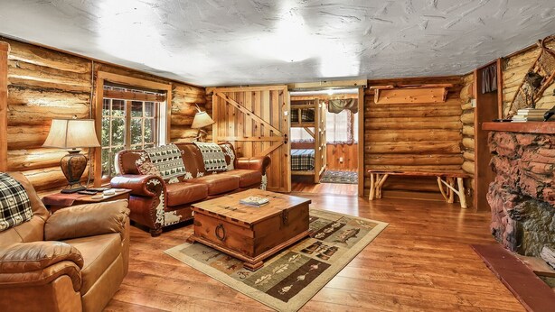 A log cabin interior with a wooden floor, a leather sofa, a wooden coffee table, and a plaid-patterned throw blanket.