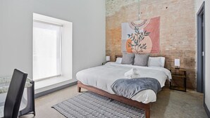 Ein modernes Schlafzimmer mit einem großen Bett, einem Fenster, einer Ziegelwand und einem Wandteppich.
