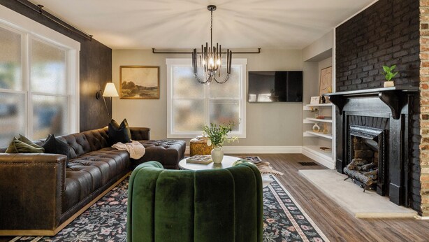 Una sala de estar con sofá de cuero, sillón verde, chimenea y candelabro.