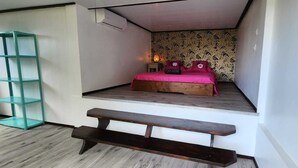 A compact bedroom with a bed, a small bedside table, a bench, and a wall-mounted shelf.