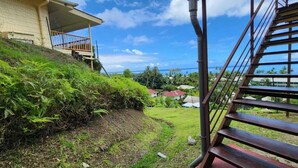 A staircase leading to a balcony overlooking a lush garden and a view of the ocean.