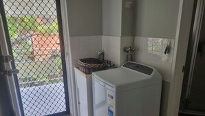 A laundry room with a washing machine, a basket on a counter, and a door leading to an outdoor area. -  Bribie Island Dreams (Bongaree)