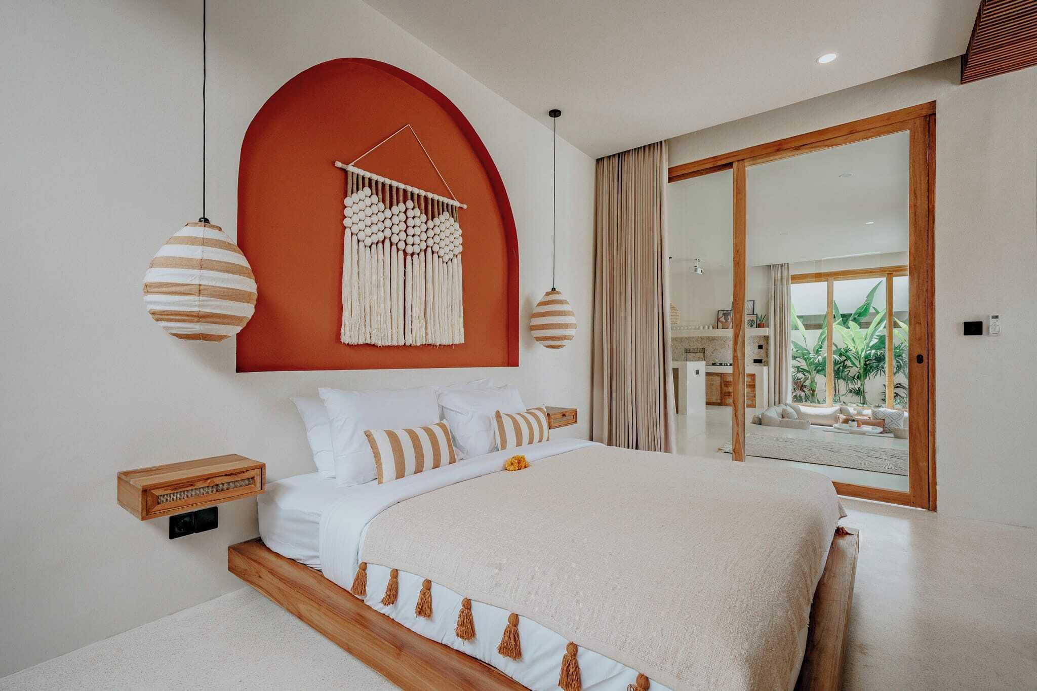 A modern bedroom with a large bed, wooden headboard, and a macrame wall hanging.